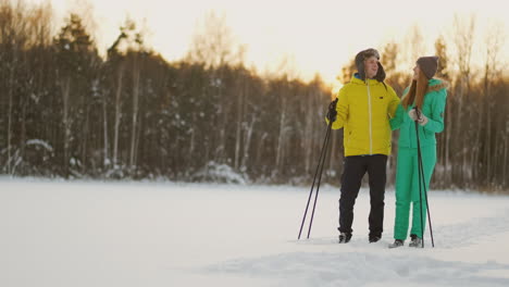 mírense con ojos amorosos mientras esquían en el bosque invernal. una pareja casada practica un estilo de vida saludable