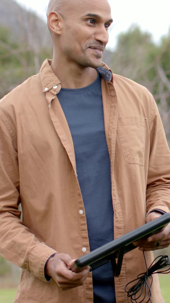 Vertical video: Right prompt causing man in tan shirt adjusting tablet and coiled cable in field
