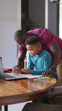 video vertical de un feliz padre afroamericano ayudando a su hijo en la tarea