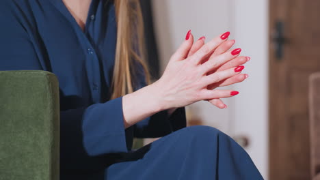 Female emotional coach wearing blue blouse seated indoors gesturing with manicured red nails while speaking to patient with wooden door in background and calm professional environment