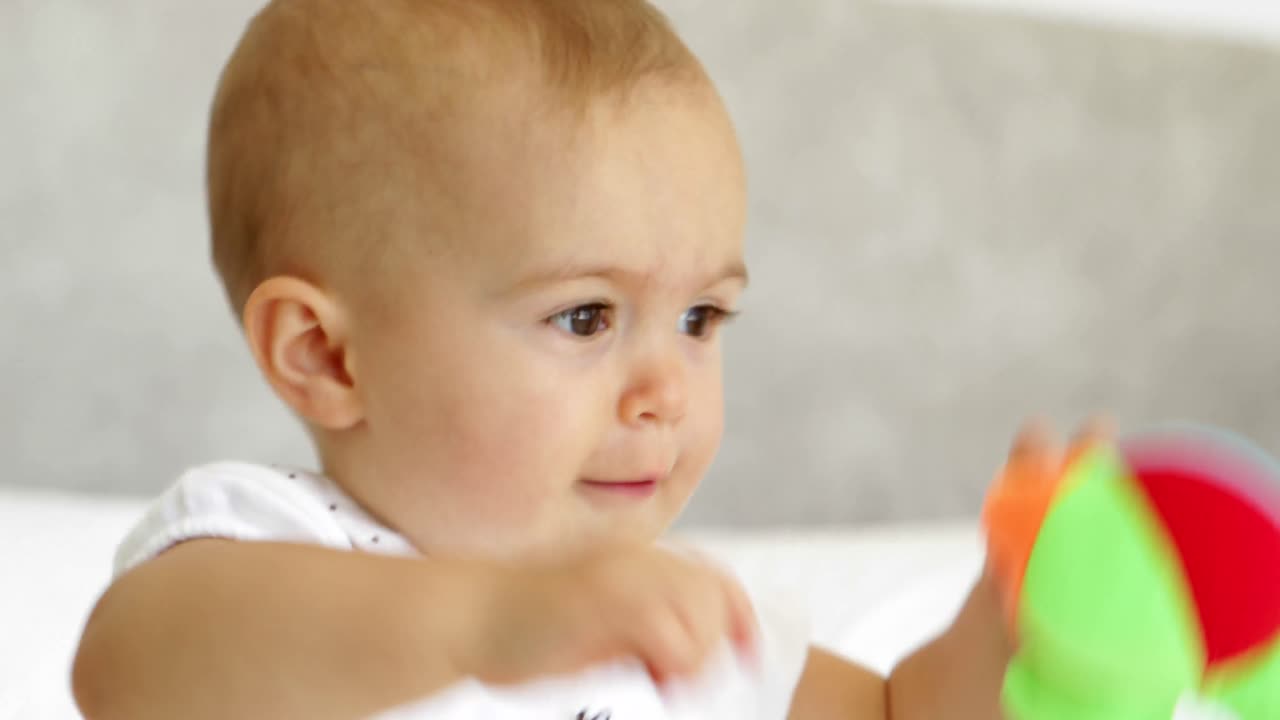 귀여운 아기 소녀가 침대에 부드러운 공을 가지고 놀고 있습니다.