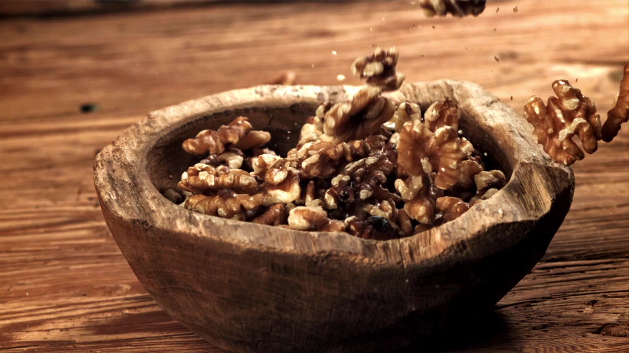 Shelled Walnuts Falling into a Rustic Wooden Bowl in Slow Motion