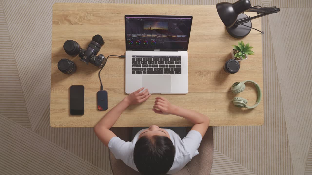 Top View Of Asian Woman Color Grading Yawning And Sleeping While Sitting In The Workspace Using A Laptop Next To The Camera Editing The Video At Home