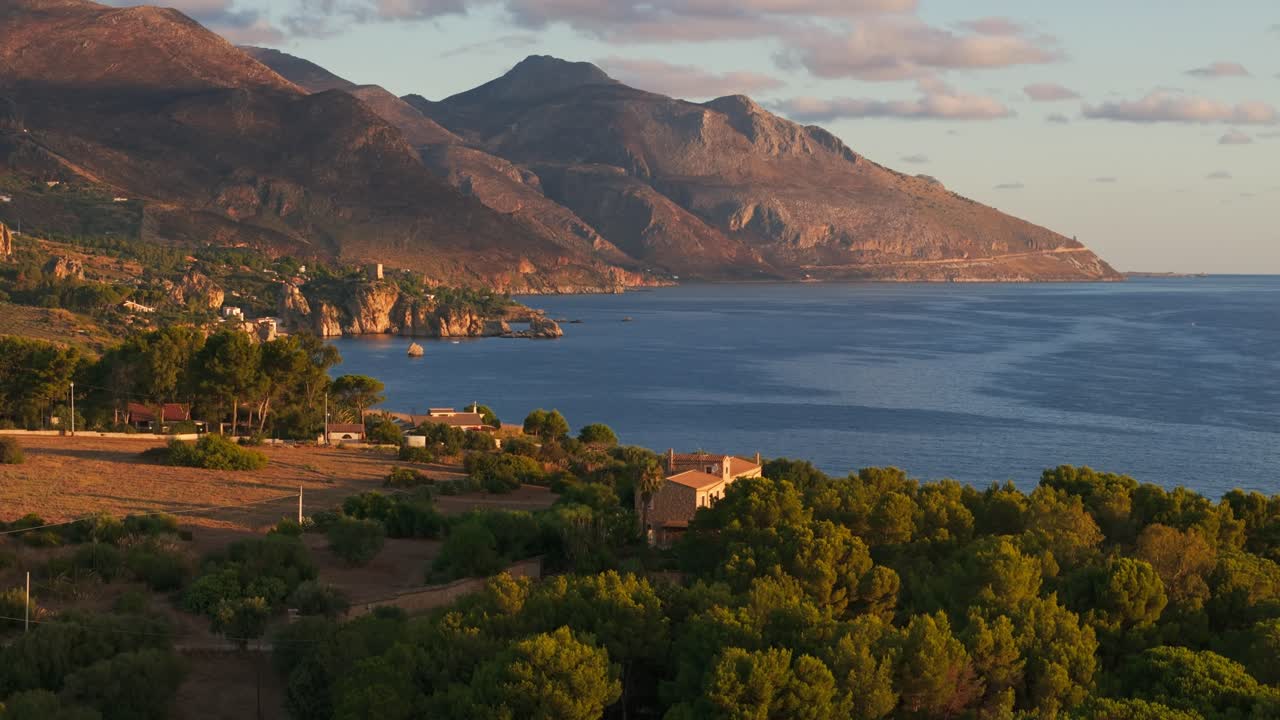 Push-in aerial drone of Guidaloca Beach and Sicilian coast in Sicily, Italy during sunrise, showing vast blue ocean, cliffs, and natural scenery