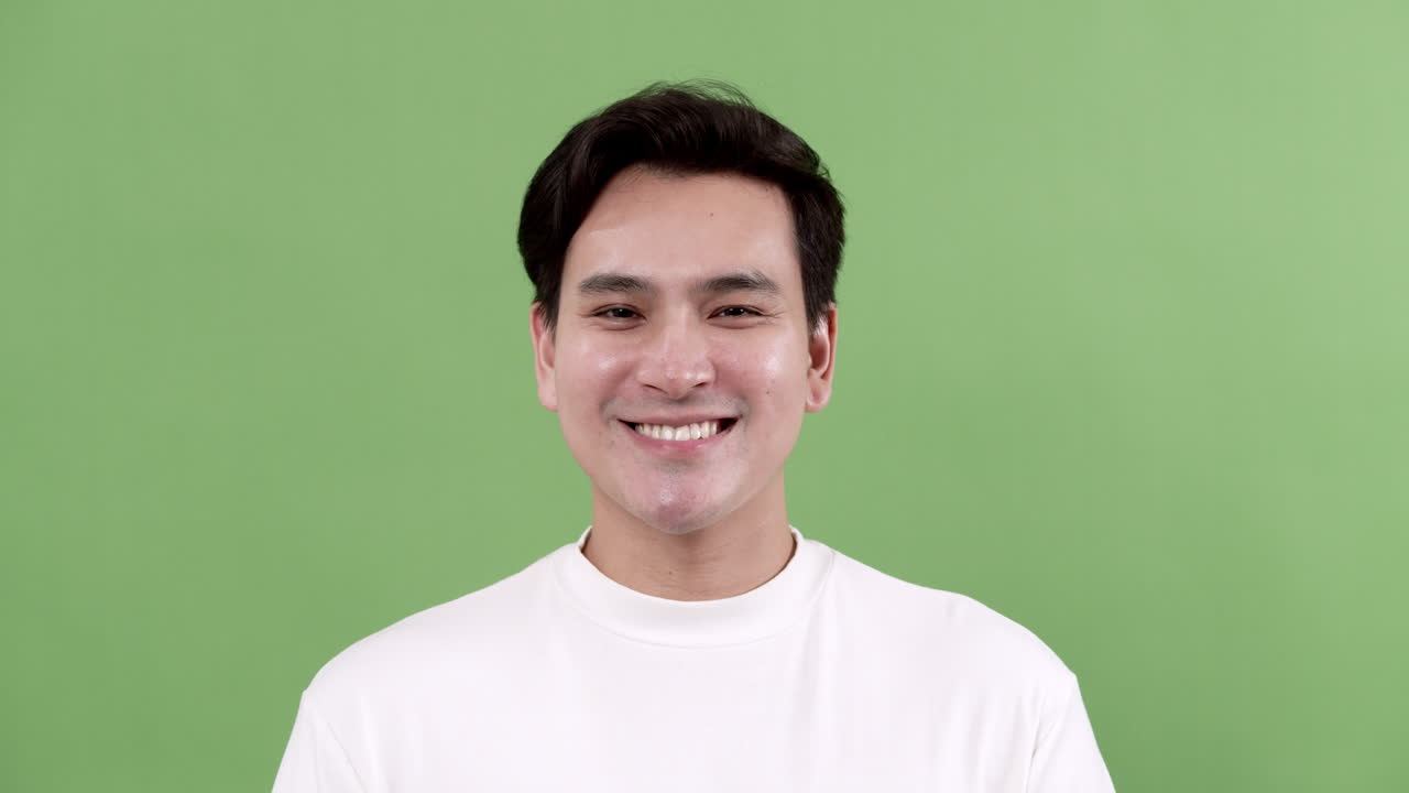 A cheerful young man smiles brightly in a studio against a vibrant green backdrop capturing pure joy.