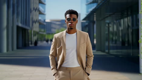 a stylish man in a beige suit and sunglasses stands confidently in a modern urban environment