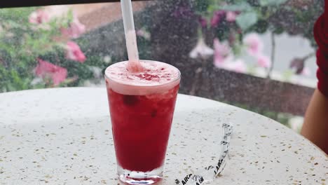 hand stirring a red drink with straw