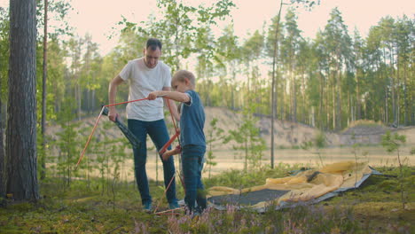 a slow-motion father and two children set up a tent in the woods during a weekend trip. fatherhood and children