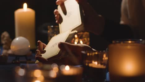 primer plano de una mujer mezclando o cortando cartas para la lectura del tarot en una mesa a la luz de las velas