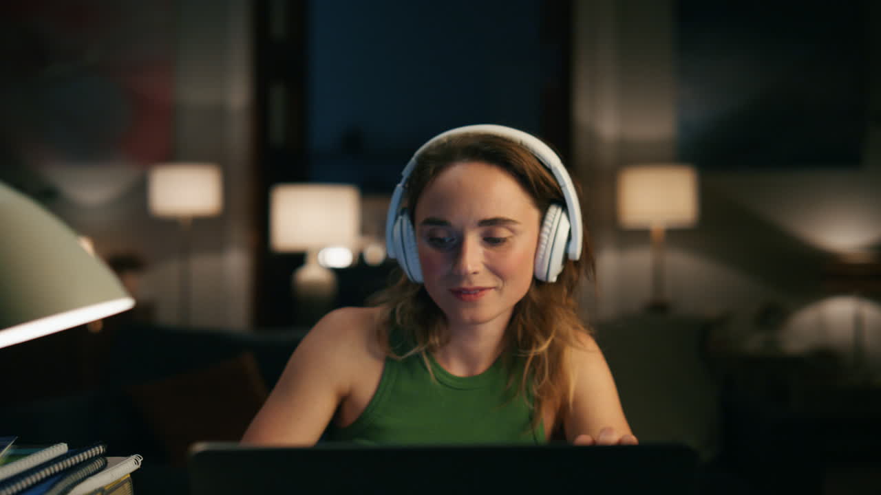 Young specialist working laptop night closeup. Headphones girl listening podcast