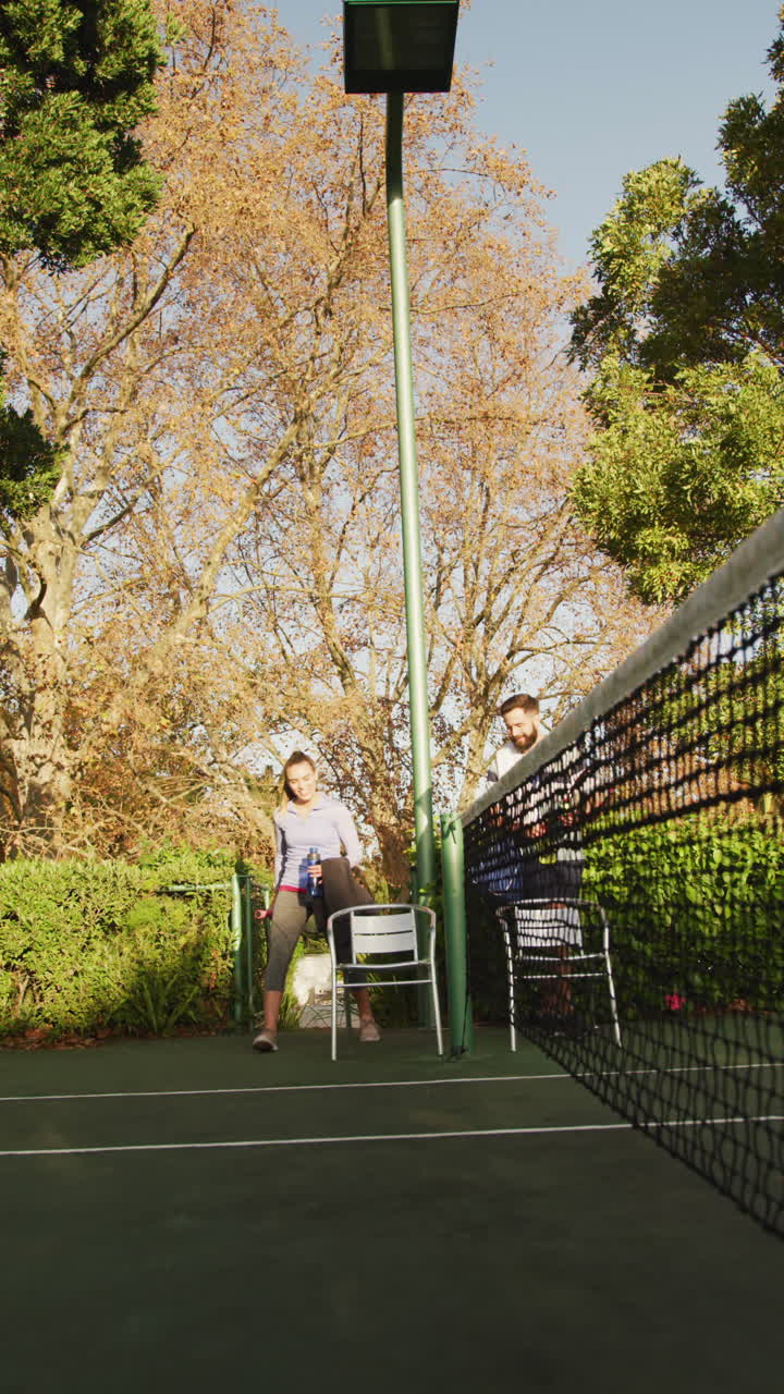 Vertical video of happy caucasian couple preparing for playing tennis