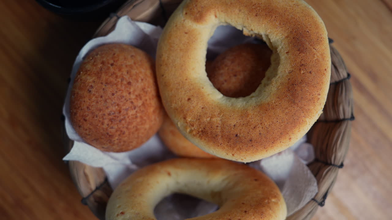 Close-up shot of soft, golden-brown Colombian almohabanas and pandebono in a woven basket. Warm, rustic lighting enhances the textures of this traditional Latin American bread
