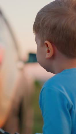 niño lava el coche de papá con pulverizador en el césped. diligente ayudante de niño pequeño vierte agua en auto sucio en el patio trasero. niño pequeño juega limpieza de vehículo