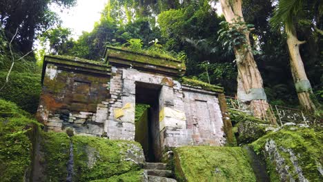 estableciendo el tiro en la antigua puerta de piedra, la entrada del templo de goa garba, bali, indonesia, alrededor del musgo, verde paisaje tropical, punto de referencia religioso