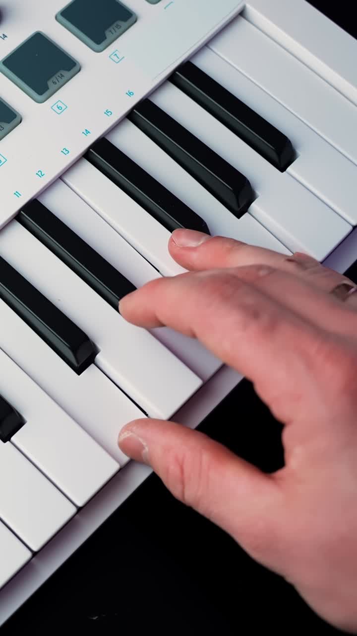 Vertical close-up of a hand playing notes on a white MIDI keyboard controller with shallow depth of field, ideal for music production, songwriting, and studio b-roll