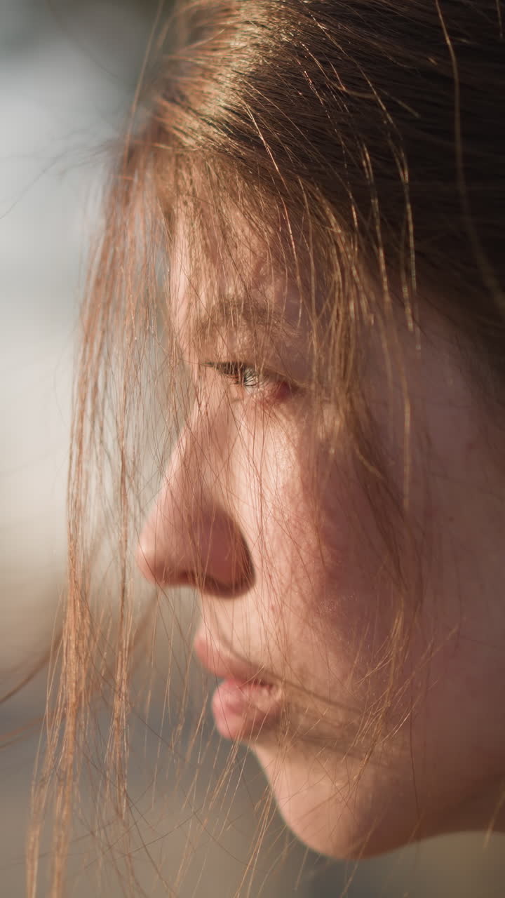 A close-up of a girl wearing a brown coat, with her hair partially covering her face. She appears tearful and lost in thought, her expression reflecting a profound sense of sadness and introspection