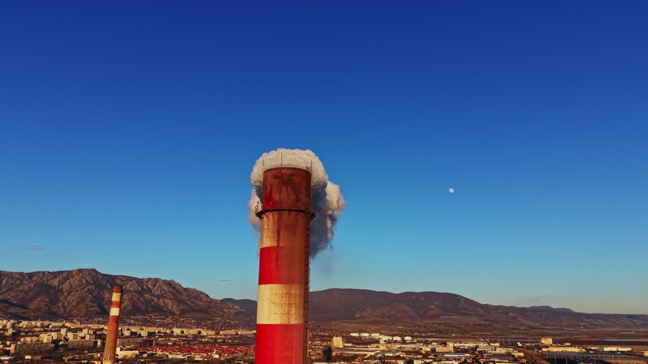 Il camino di una fabbrica rilascia fumo sul paesaggio nel pomeriggio