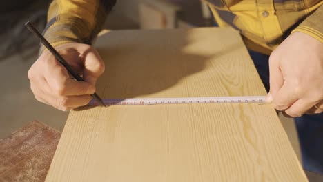 el carpintero mide la madera cruda con el medidor y marca los lugares medidos con un lápiz.