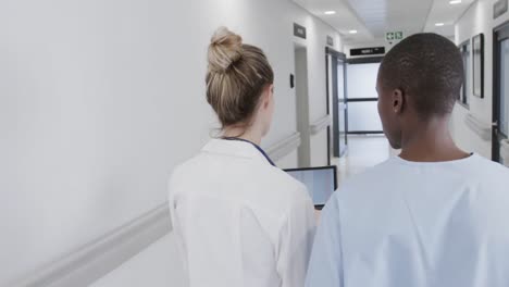 diverse female doctor and nurse in hospital corridor, using tablet and talking, in slow motion