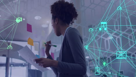Animation of network of connections with icons over african american businesswoman in office