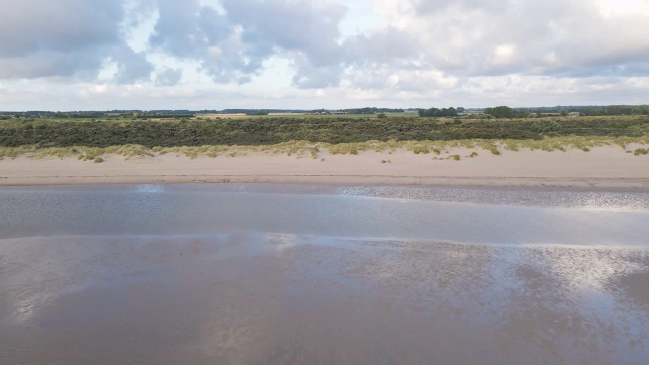 ondas aéreas de sobrevuelo del mar del norte que llegan a la costa con playa de arena y paisaje escénico en el fondo