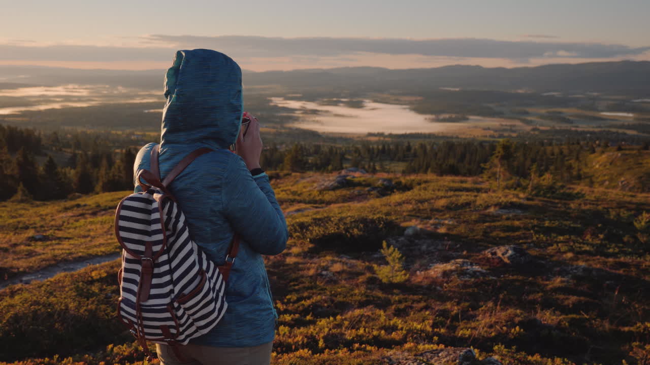 el hombre de la capucha está descansando en la cima de la montaña bebiendo café caliente de una taza calentando su
