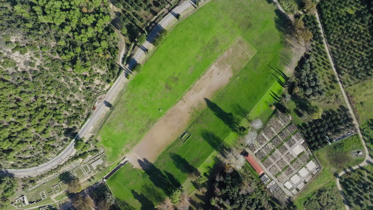 Aerial orbit descend on Olympia stadium and adjacent ruins in lush Greek forest region