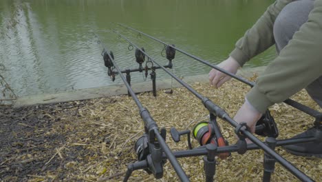 close up shot of male hands setting up a fishing rod and spinning reel with lake water in the background at daytime