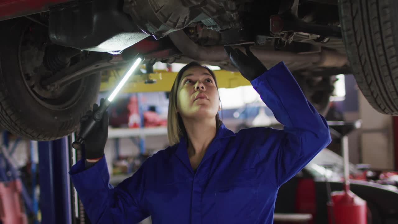mecánica femenina usando una lámpara led y trabajando debajo de un automóvil en una estación de servicio de automóviles