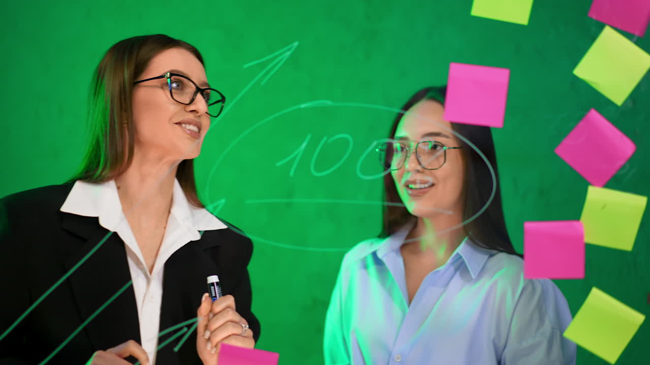 Business ladies look at the glass board with stickers on. Communication, cooperation and building strategies.