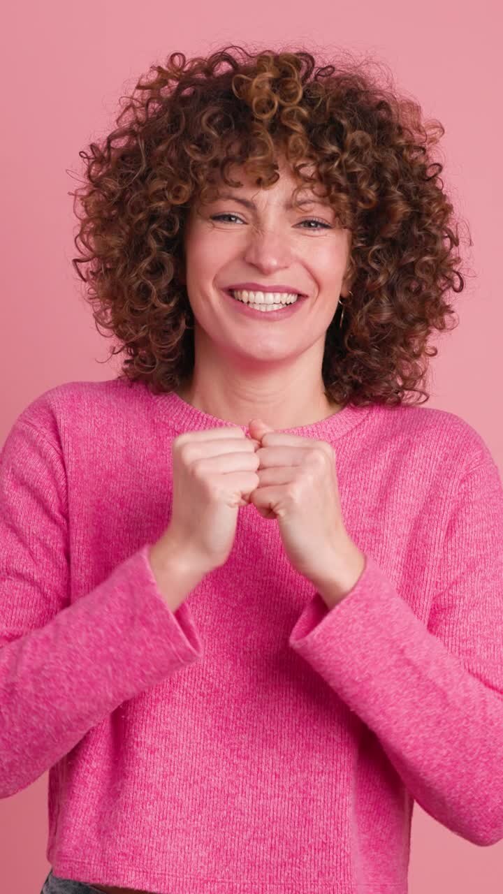 Giovane donna entusiasta che batte le mani e sorride su sfondo rosa. Filmato verticale.