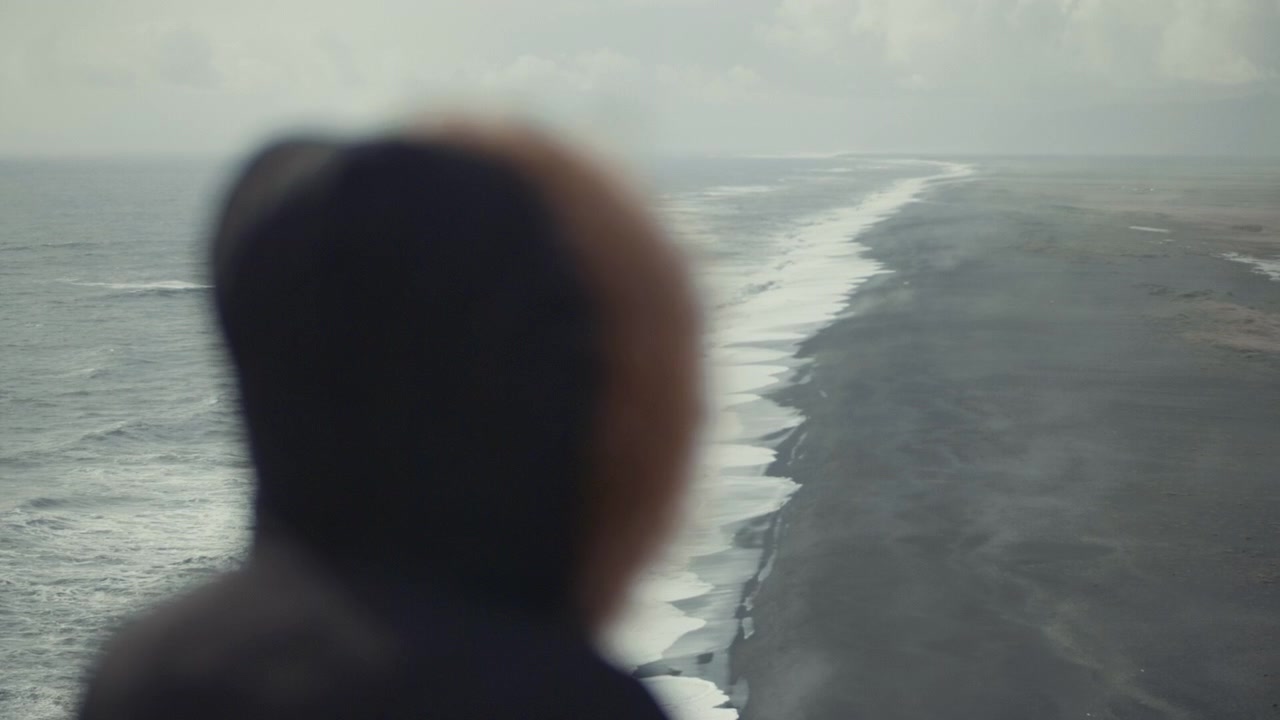 Person in Hooded Jacket Looking at a Black Sand Beach and Ocean