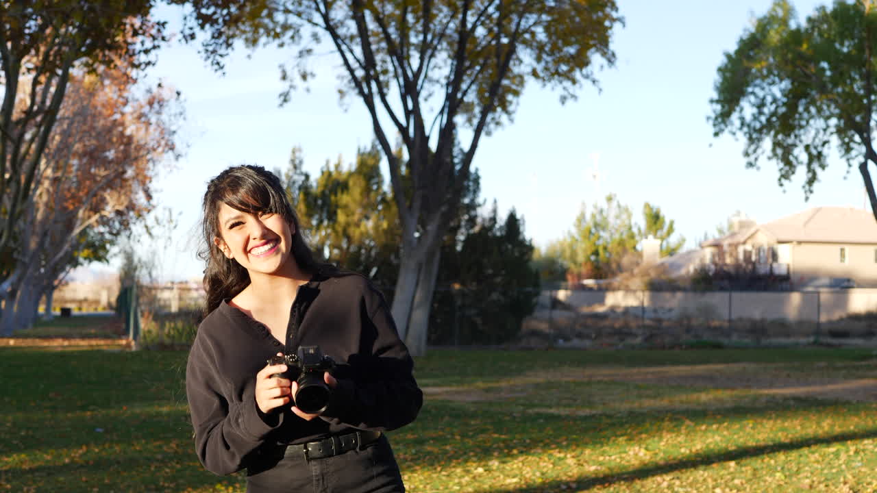 una bella fotógrafa tomando una foto en un parque al atardecer con una cámara digital sin espejo mientras sonríe y ríe