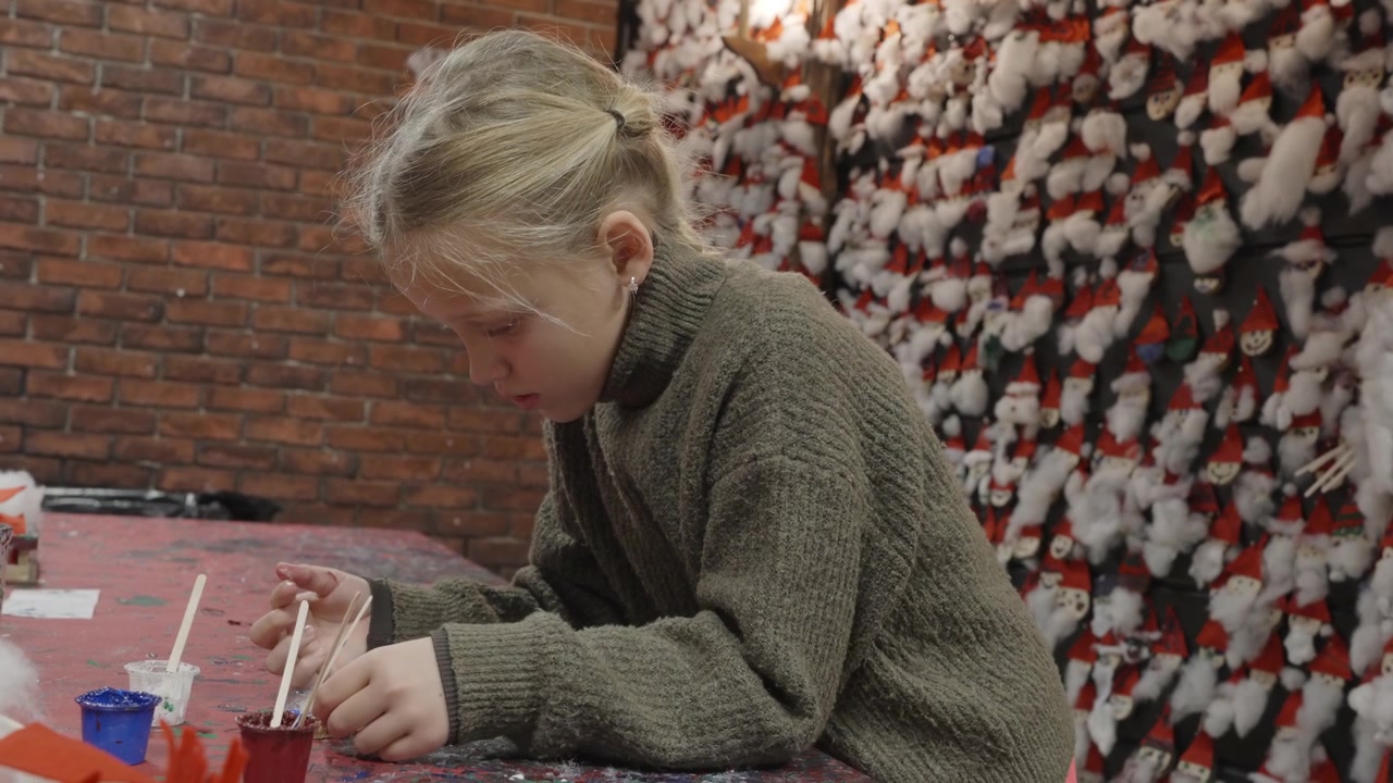 A nine year old girl makes festive Christmas crafts at a workshop table inside Santa Claus Village in Rovaniemi, Finland, surrounded by handmade ornaments on the wall
