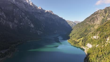 Majestic-aerial-view-of-Klöntalersee-with-Vorderglärnisch-peaks-in-Glarus,-Switzerland,-on-a-sunny-day