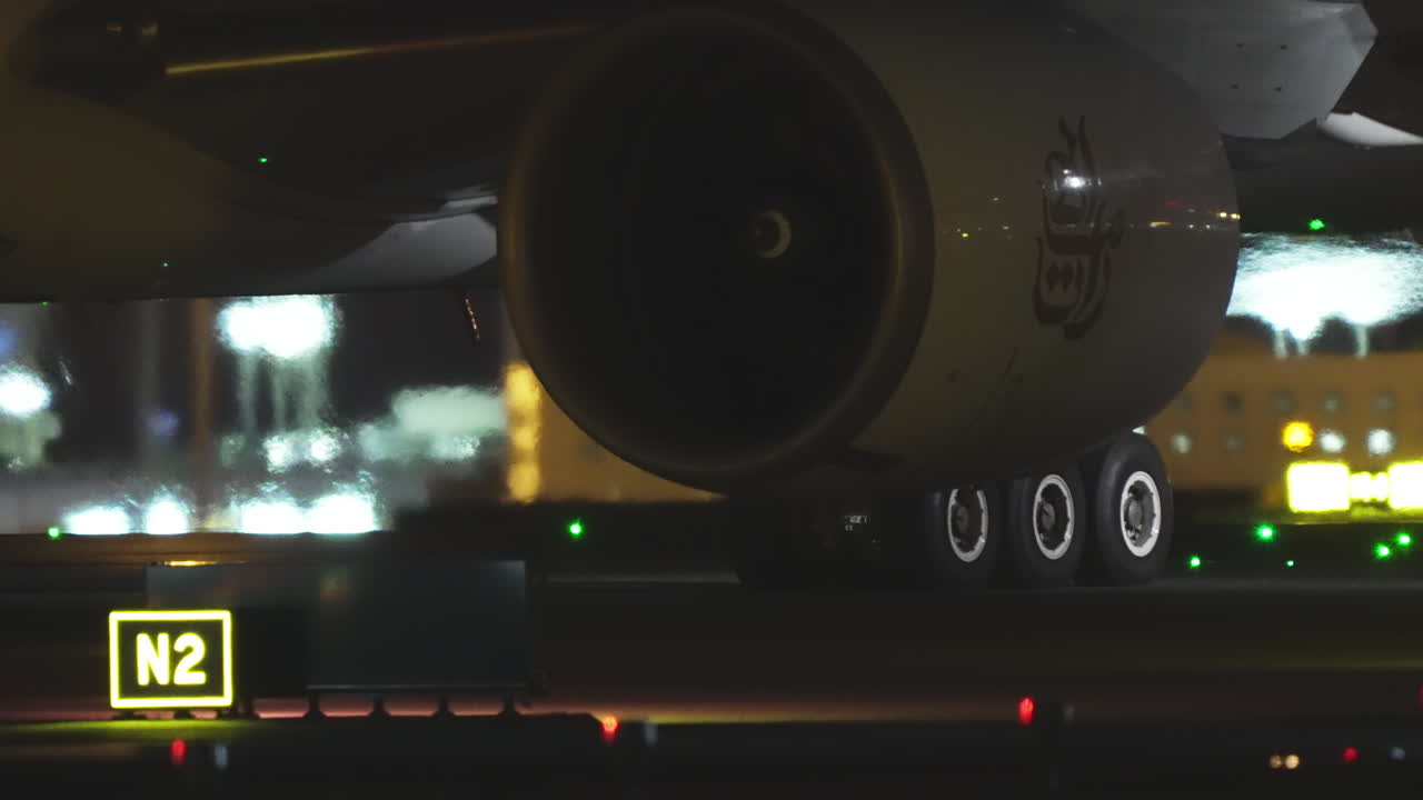 Carrello di atterraggio principale e motore di un aereo in primo piano di notte, con il segnale della via di rullaggio N2