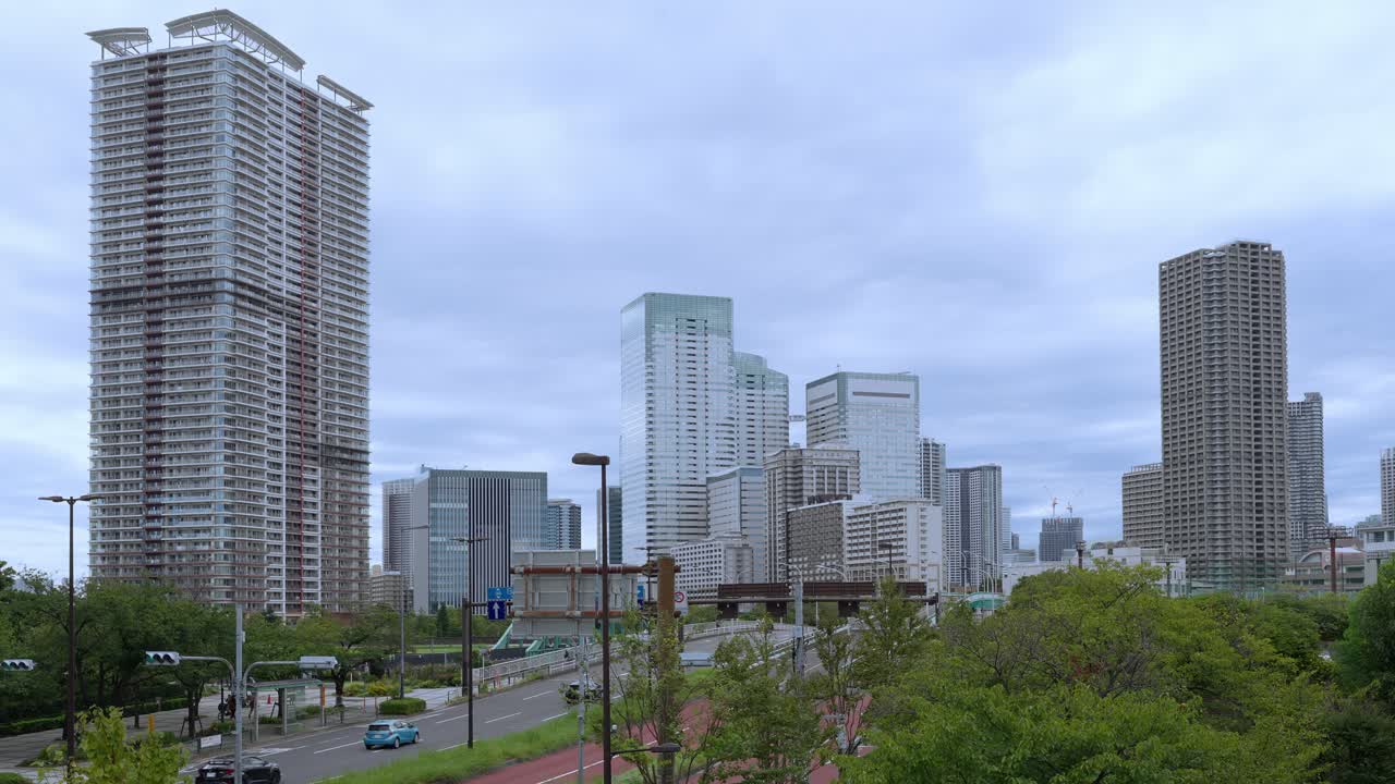 A wide shot of the Tokyo skyline with tall modern skyscrapers against a dramatic, cloudy sky