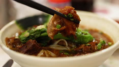 chopsticks lifting meat from noodle bowl