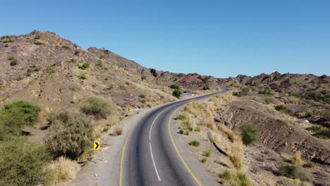 Vista-Aérea-De-La-Carretera-Vacía-De-Rcd-A-Través-De-Baluchistán-Que-Serpentea-A-Través-Del-Paisaje-Rocoso-Del-Desierto