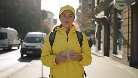 a young woman in bright yellow outerwear stands confidently on a sunny street, holding a package, showcasing urban life and modern style