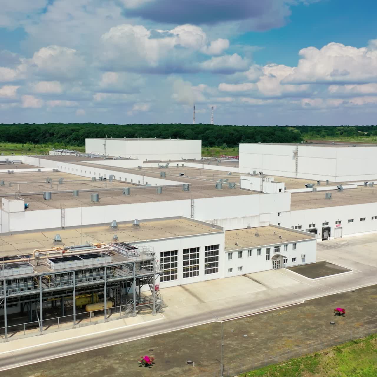 Exterior of industrial complex in the countryside. Modern buildings with parking for trucks among green fields under blue sky in summer