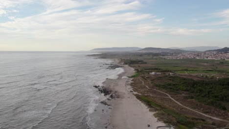 sandy coastline in minho, northern portugal, with gentle waves meeting the shore and distant mountains visible on the horizon - drone