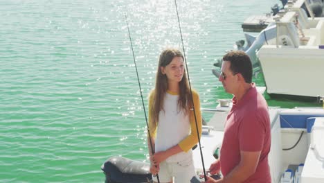 side view of a caucasian man and his teenage daughter holding fishing rods