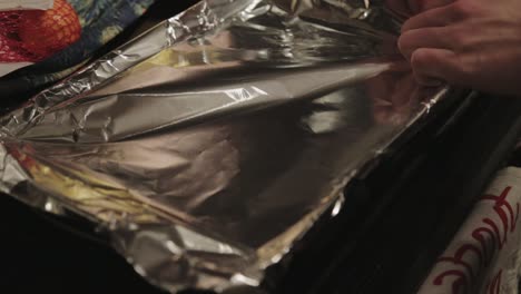 chef covering the baking pan with aluminum foil wrap - closeup shot