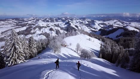 Rising-up-as-two-people-descend-along-a-snow-covered-ridge-on-Hundwiler-Hoehe,-Swiss-Alps,-aerial