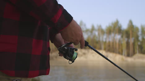 pescador está girando el carrete de la caña de pescar vista de cerca de las manos de pesca y la pesca de giro en el lago de bosque