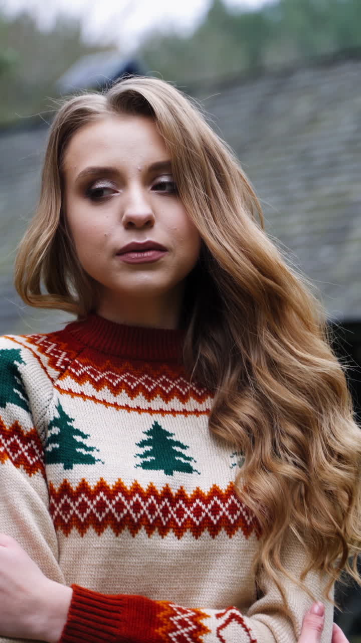 Attractive girl outdoors. Beautiful young woman in knitted Christmas sweater standing alone in the village in cold autumn season. Vertical video