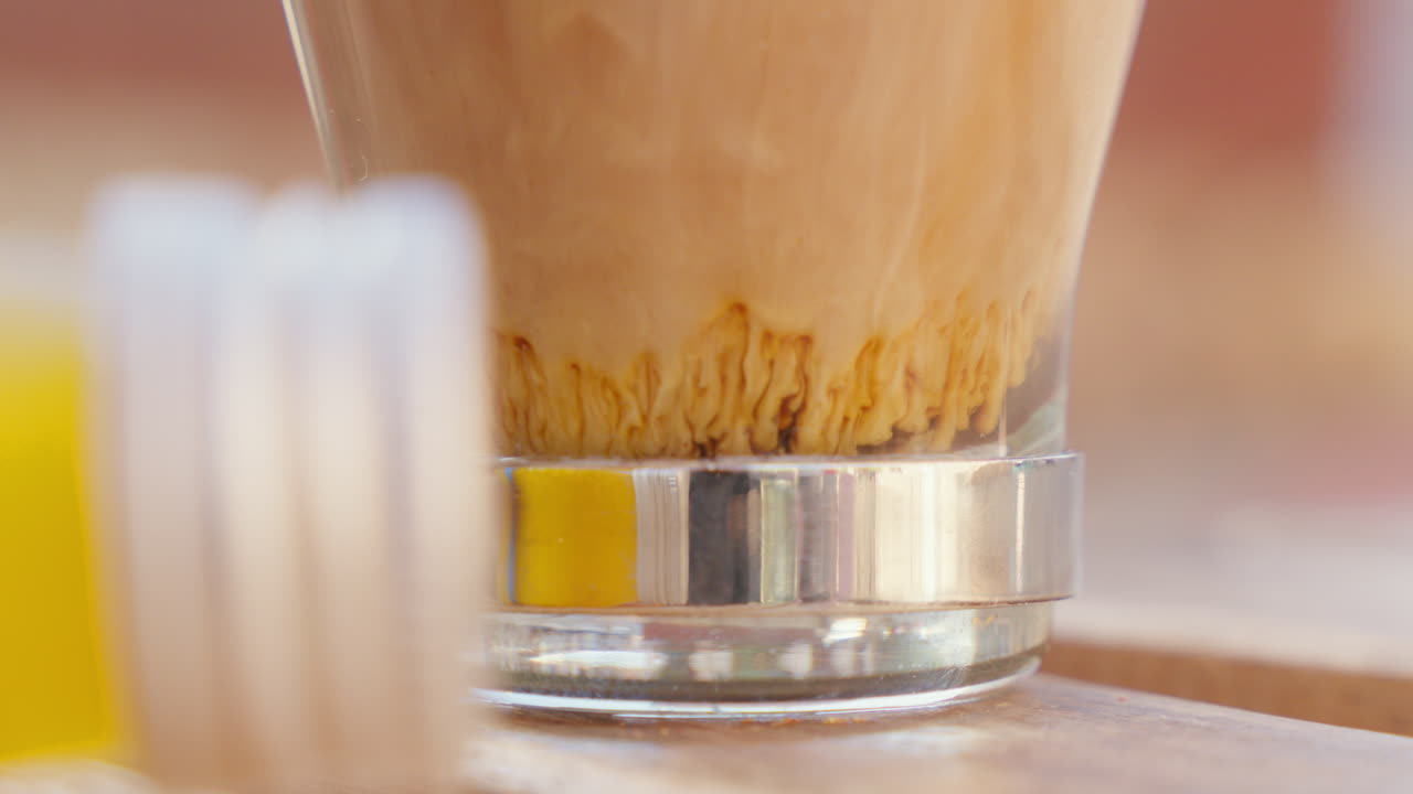 A close-up view of milk merging with coffee, creating an appealing pattern in an outdoor caf&eacute; setting