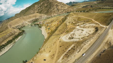 el río serpenteante serpentea a través del valle. las orillas adyacentes a la carretera que conducen al campamento turístico anidado en el abrazo de las tierras altas. los acantilados altísimos