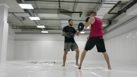 slow motion: power blow to boxing paw. strong tattooed athlete in sports clothing training on boxing paws with partner